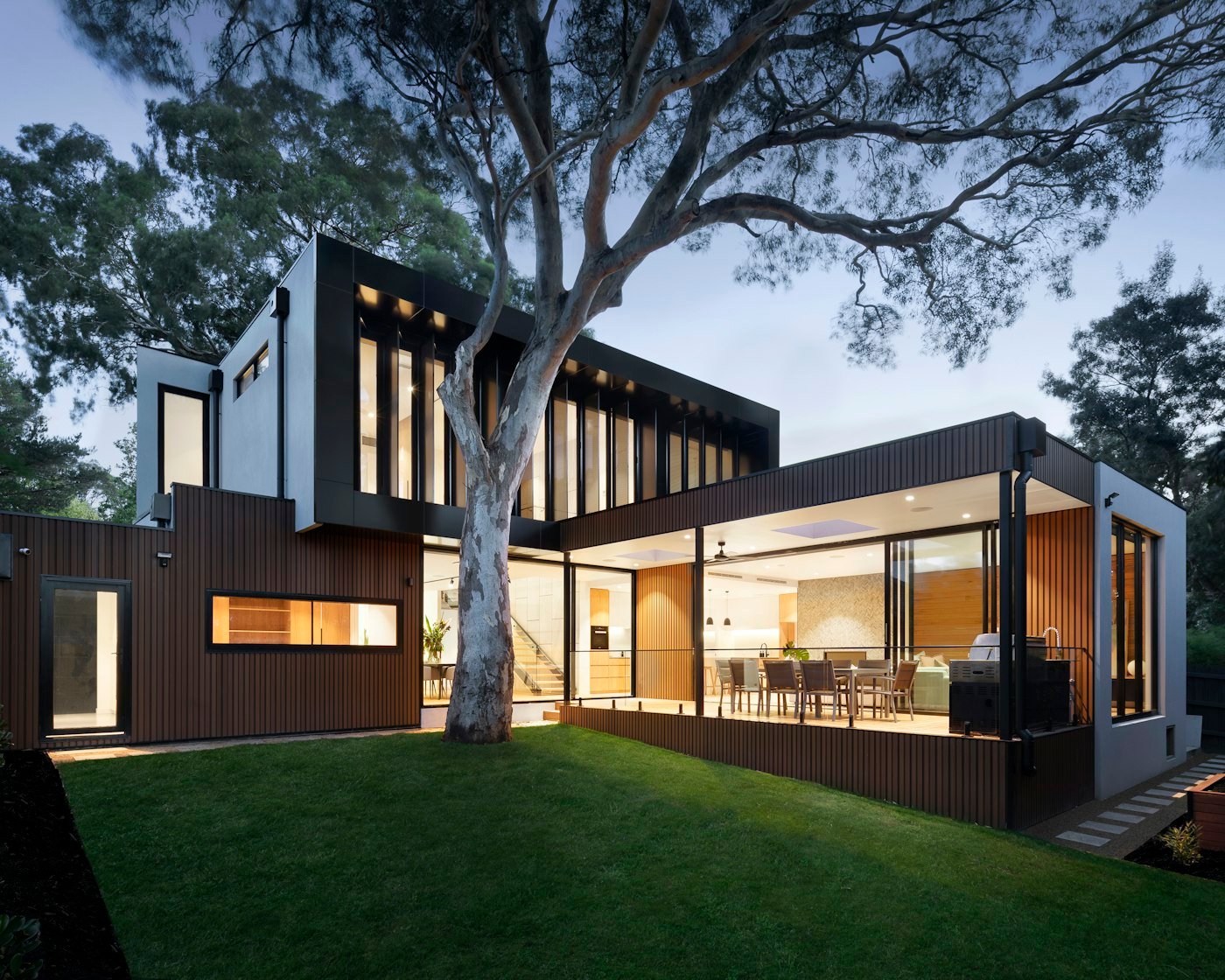 Modern house at dusk with large glazed doors and windows opening onto the garden